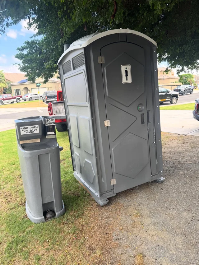 A freestanding handwashing station next to a portable restroom